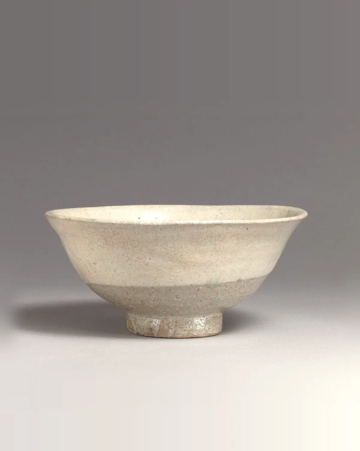 A wide tea bowl in pale buncheong slip on a tall foot